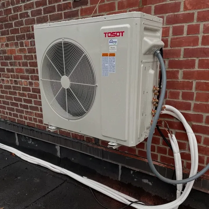 TOSOT outdoor unit against brickwork with connected lines.